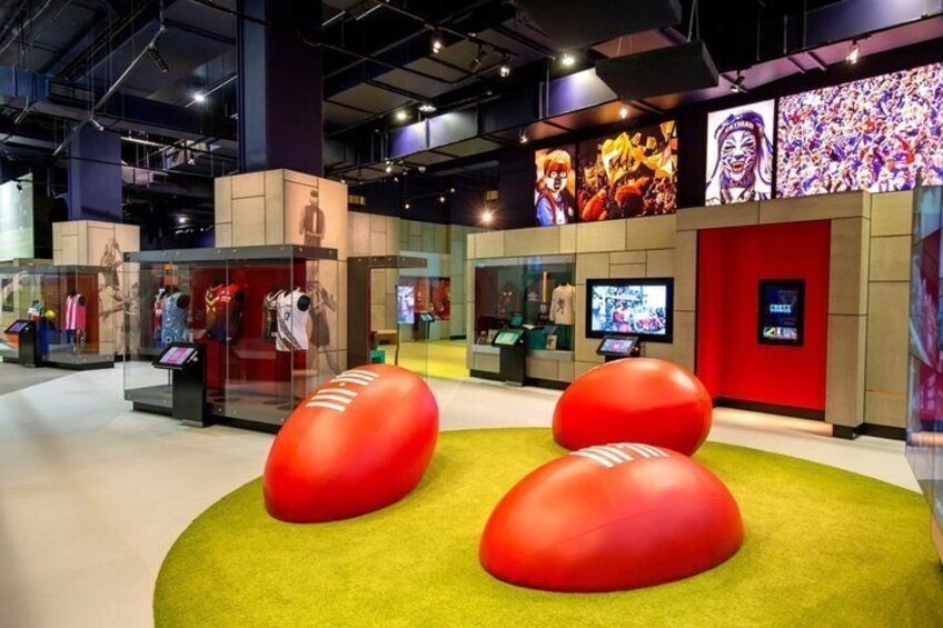 A museum interior with glass display cases, red spherical objects on a green carpet, and digital screens on the walls. 3