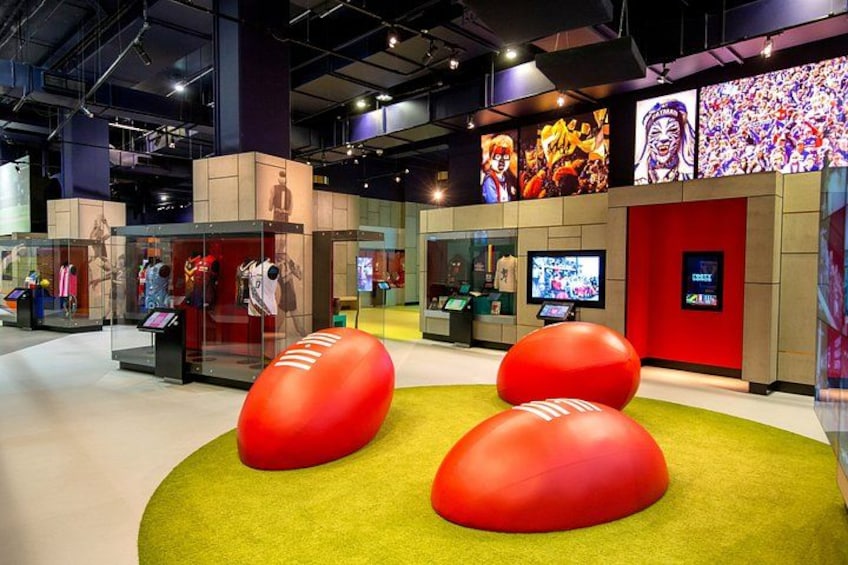 A museum exhibit with red spherical objects on a green carpet, glass display cases, and digital screens. 2