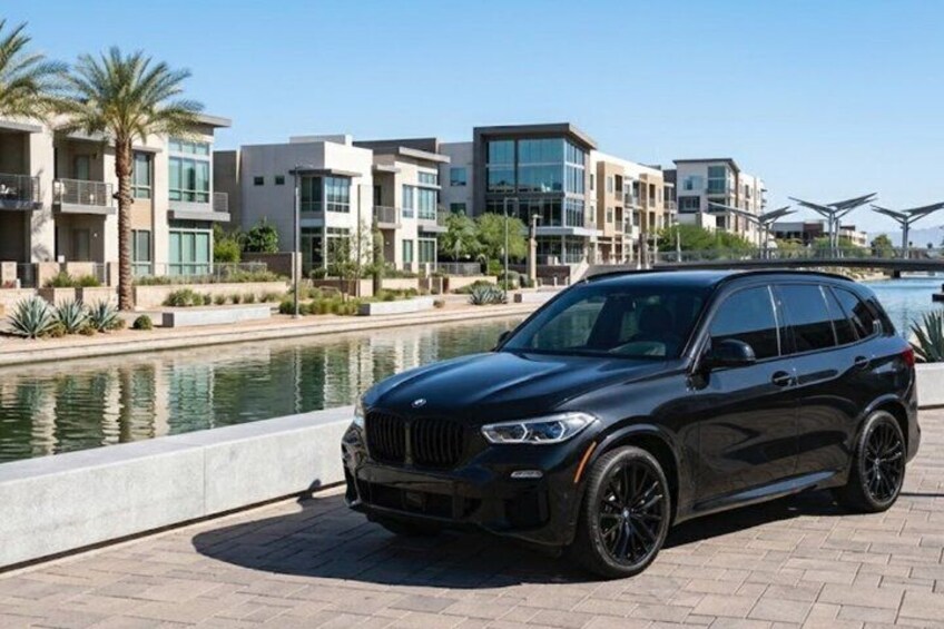 A black SUV parked by a waterfront with modern buildings in the background. 5