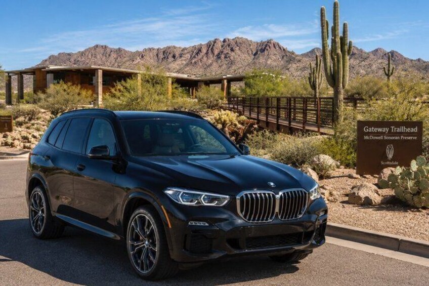 A black BMW SUV parked in a desert setting with a sign reading 'Gateway Trailhead McDowell Sonoran Preserve.' 4
