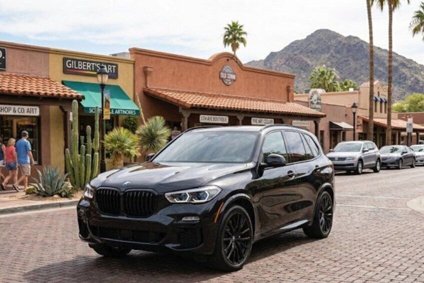 A black BMW SUV parked on a cobblestone street with shops and palm trees in the background. 1