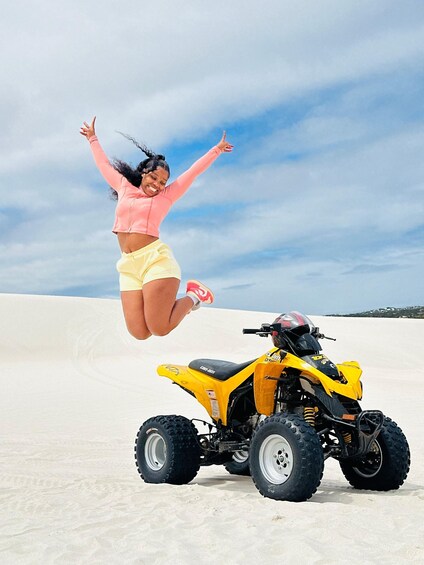 A person jumping in the air with a yellow quad bike on a sandy beach. 1