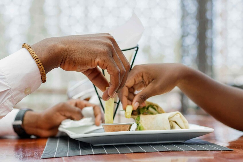 A person holding a napkin, a plate with a wrap, and a small cup, likely in a restaurant setting. 5