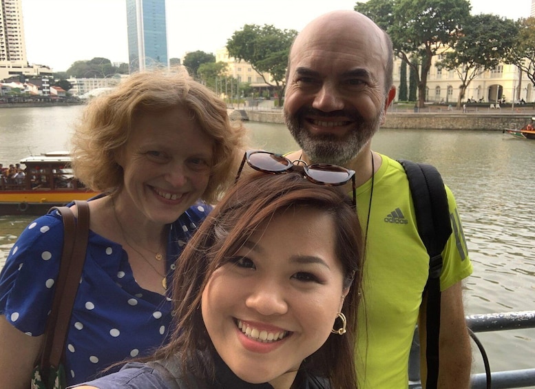 Three people near a river with buildings and trees in the background. 3