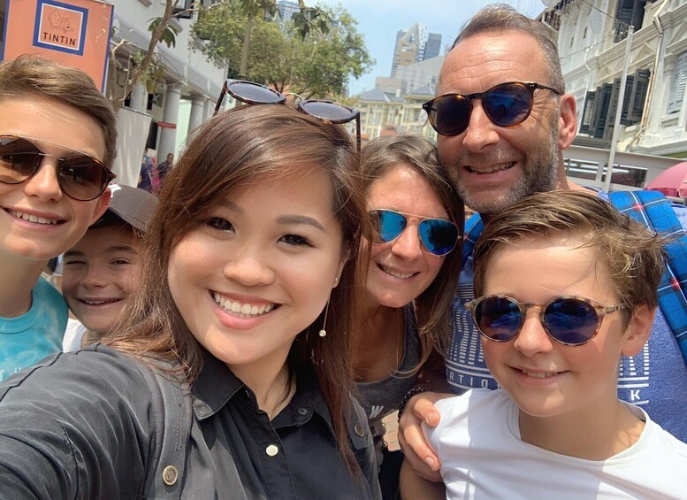 A group of people taking a selfie on a city street with buildings and a sign that reads 'TINTIN' in the background. 2