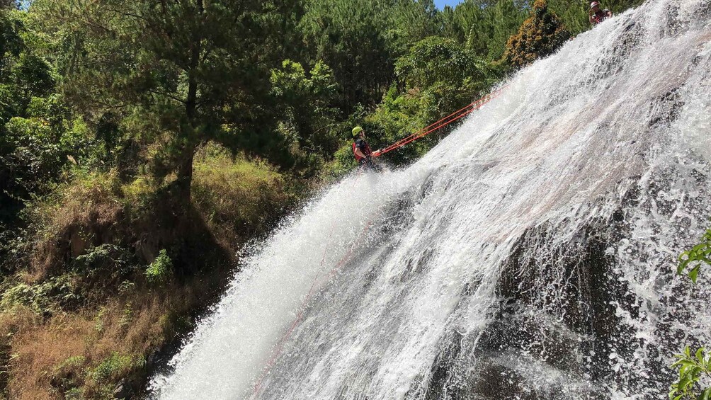 A person rappelling down a waterfall surrounded by dense forest. 4