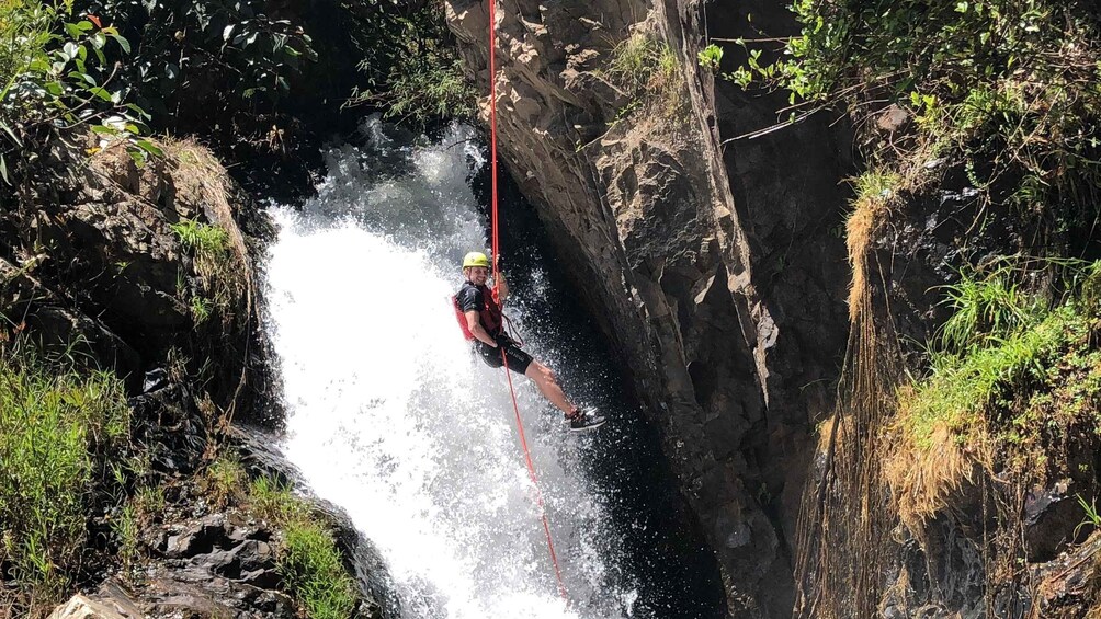 A person rappelling down a rocky cliff with a waterfall. 5