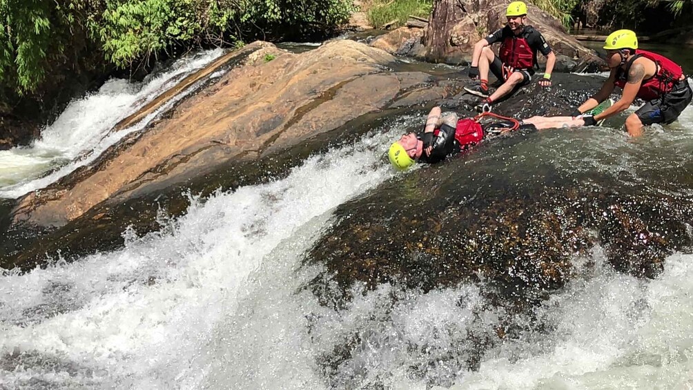A white-water rafting scene with a person in a yellow helmet and red life jacket being assisted by two others. 2