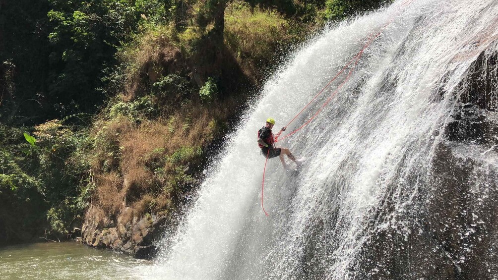 A person rappelling down a waterfall surrounded by greenery. 3