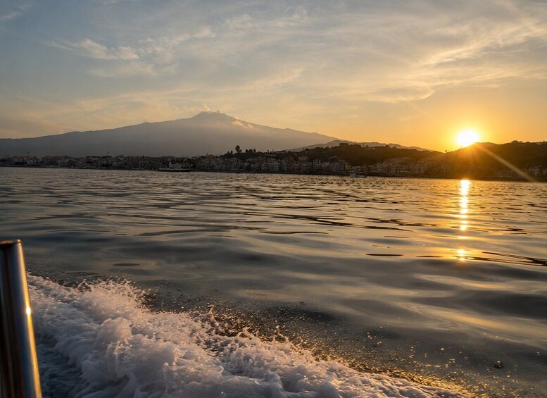 A calm body of water with a mountain in the background and the sun setting on the horizon. 5