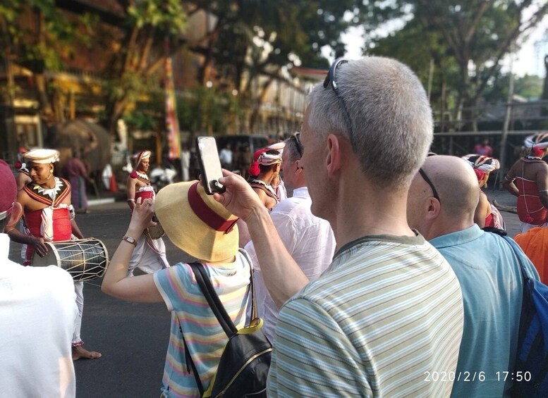 A person taking a photo of a street parade with musicians and dancers in traditional attire. 1