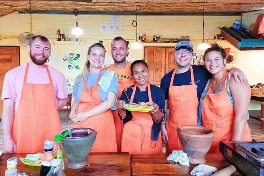 A group of people in aprons standing around a table with cooking utensils and a large pot. 3