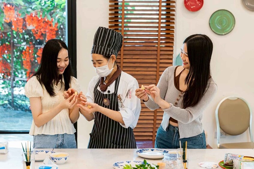 Three people in a kitchen, one wearing a chef's hat, preparing food. 1