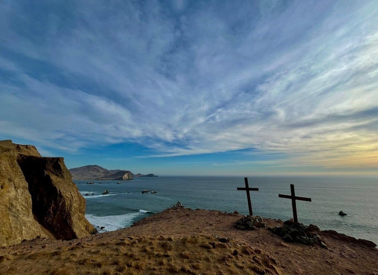 A coastal landscape with two crosses on a rocky outcrop and a large rock formation on the left. 4