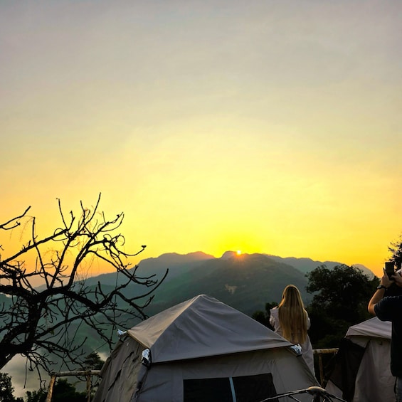 A sunset over mountains with tents and a person taking a photo. 3