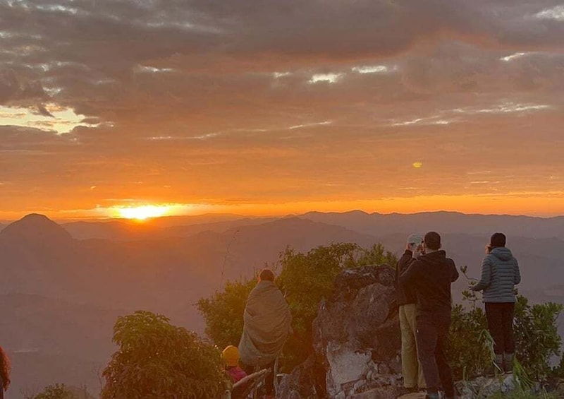 A group of people observing a sunset over a mountainous landscape. 1