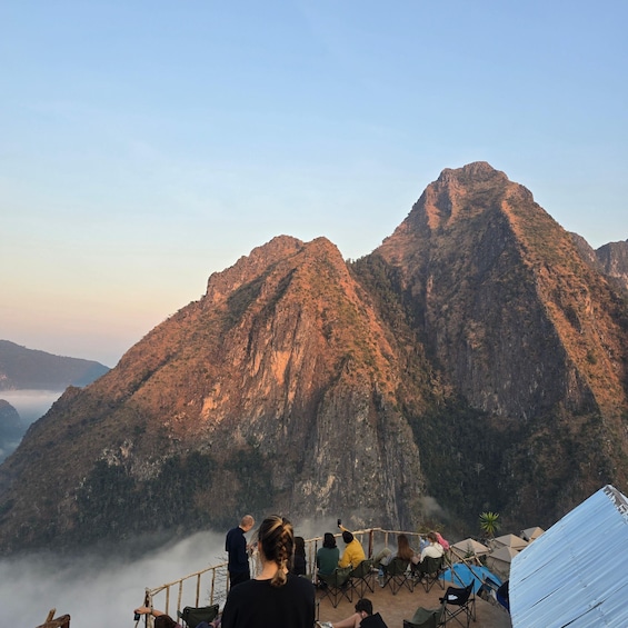 A group of people at a mountain viewpoint with a clear sky and a forested mountain in the background. 4