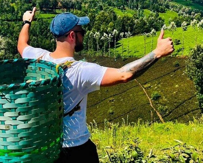 A person with a backpack and a green woven basket, standing on a hillside with a view of a green valley. 3