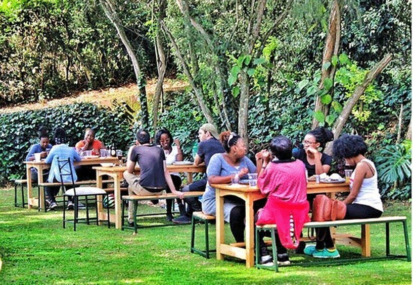 People sitting at wooden tables outdoors in a garden. 2