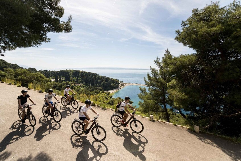 Cyclists on a paved path with a scenic view of a lake and forest. 1