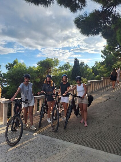Four people on a bridge with bicycles, surrounded by trees and a partly cloudy sky. 2