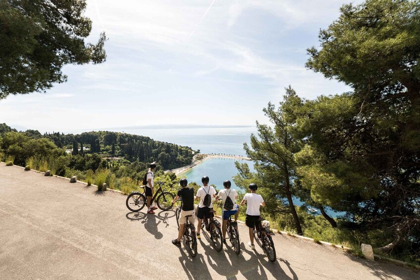 A group of cyclists on a paved path overlooking a coastal area with a clear view of the sea and a distant bridge. 5