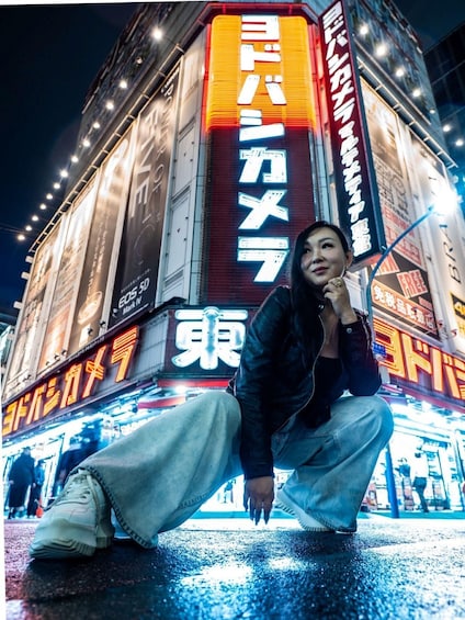 A person crouching in front of a brightly lit building with neon signs. 2