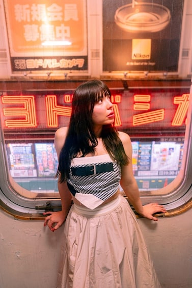 A person standing in front of a subway train window with neon signs and advertisements. 3