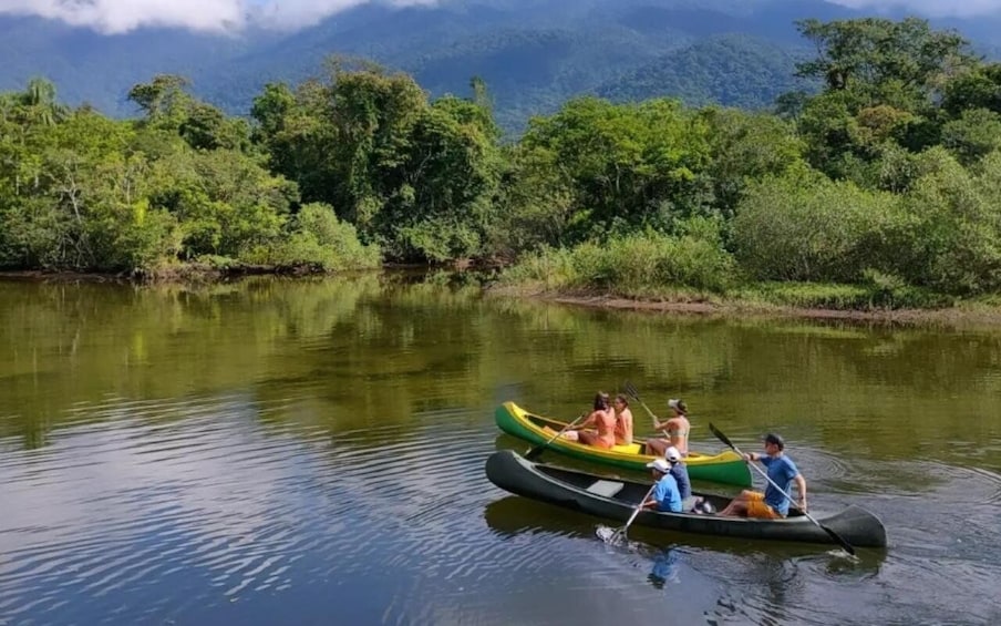 A group of people in a green canoe on a calm river surrounded by lush greenery and mountains. 1