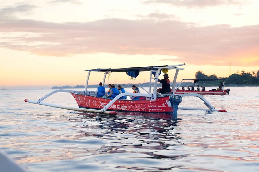 A red boat with passengers on a calm body of water during sunset. 1