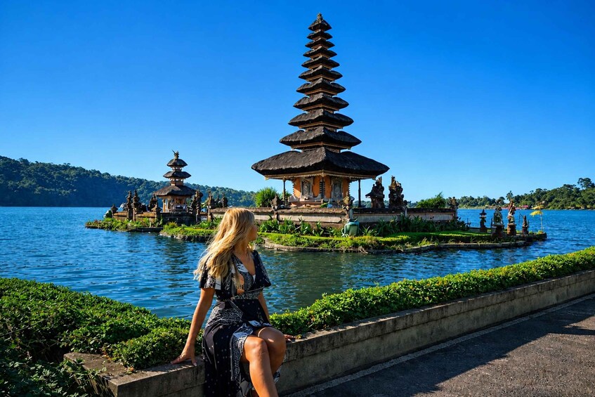 A woman sitting by a water body with a pagoda and a temple in the background. 1