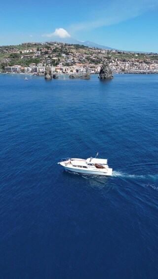 A white yacht sailing on a deep blue sea with rocky outcrops and a coastal town in the background. 5