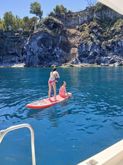 Two people on a paddleboard in a body of water with rocky cliffs in the background. 4