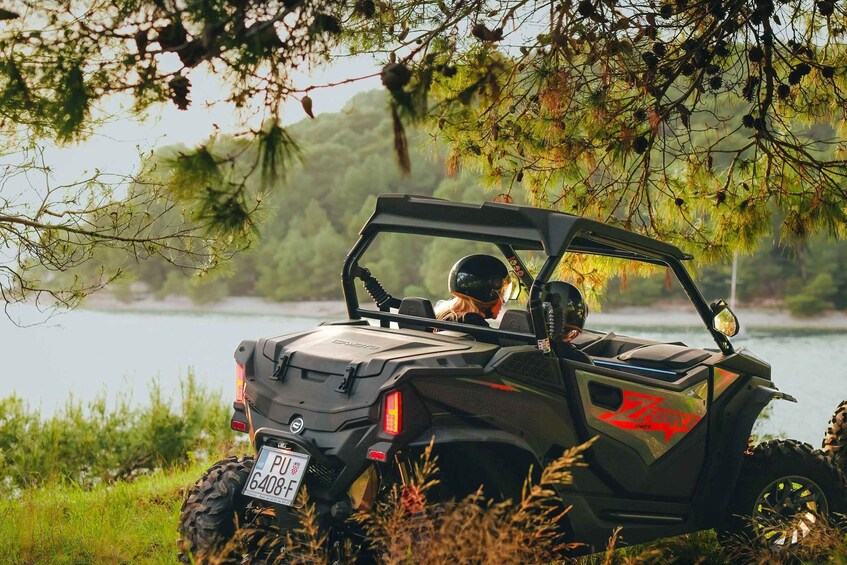 A Polaris RZR on a grassy path with a lake and trees in the background. 4