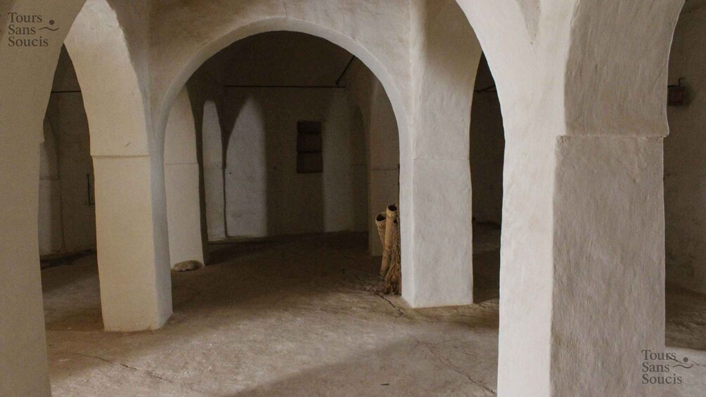 An interior with arches, a wooden post, and a tiled floor. 1