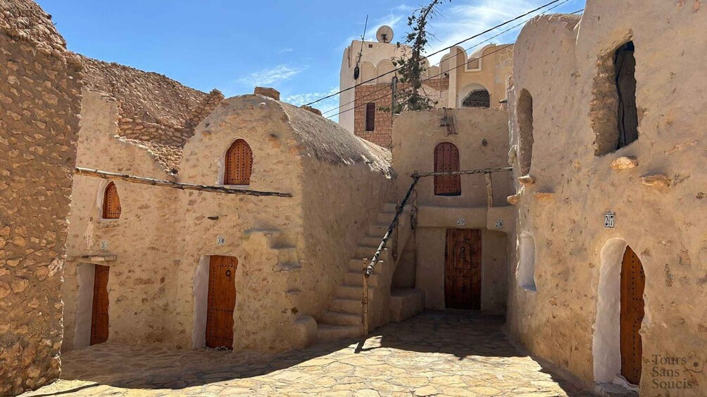 A narrow alley with stone buildings, wooden doors, and a staircase leading to a higher level. 5