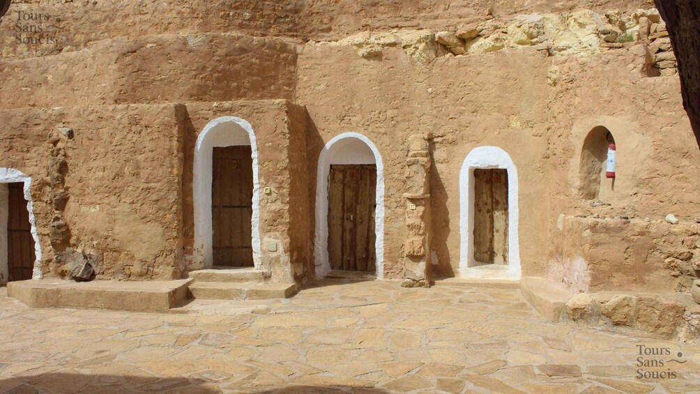A stone courtyard with arched doorways and a rustic building facade. 2