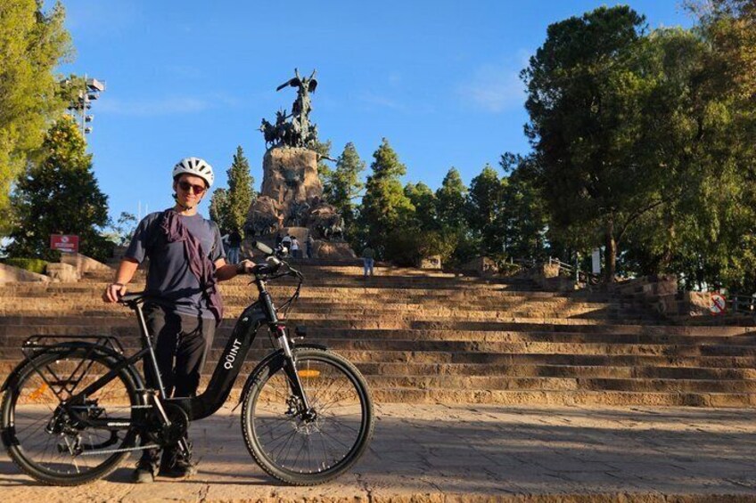 A person standing next to a bicycle in front of a statue on a stone staircase. 2