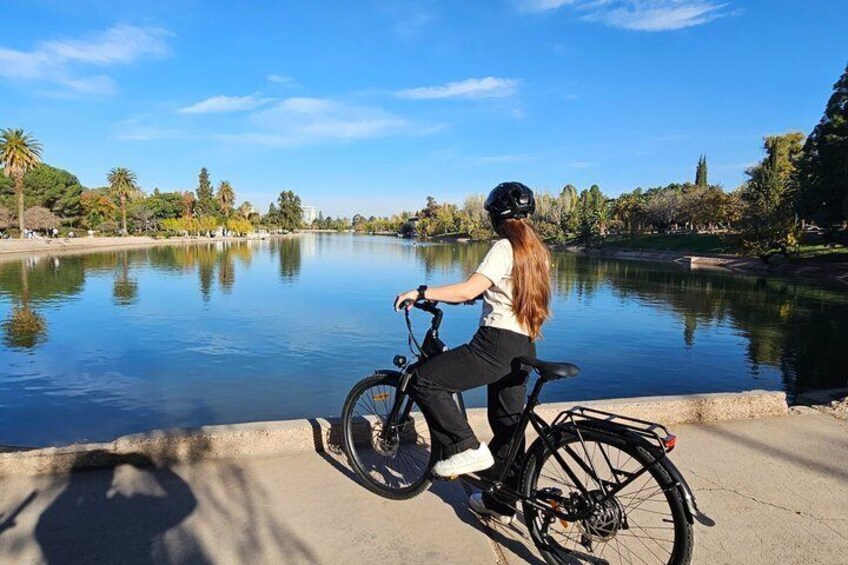 A person riding a bicycle by a calm lake with trees and a clear sky in the background. 1