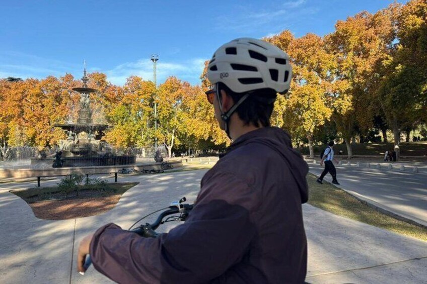 A person on a bicycle in a park with a fountain and autumn trees. 4