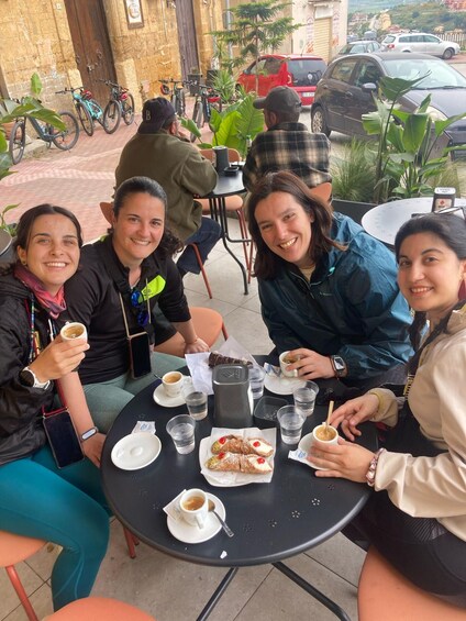 A group of people sitting at an outdoor table with food and drinks, surrounded by bicycles and parked cars. 5