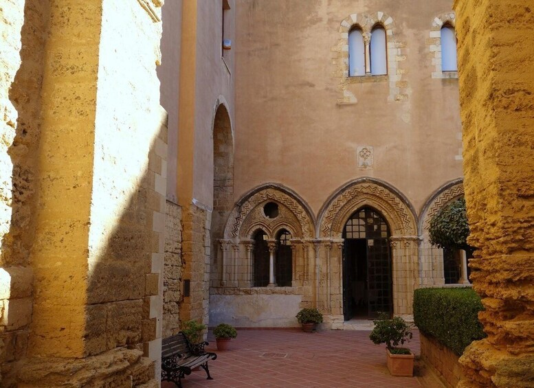 An ancient courtyard with stone arches, a bench, and potted plants. 2