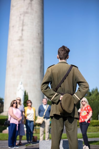 A person in a military uniform standing with hands on hips, facing a tall monument. 5