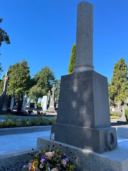 A gravestone with inscriptions, surrounded by trees and other gravestones in a cemetery. 4