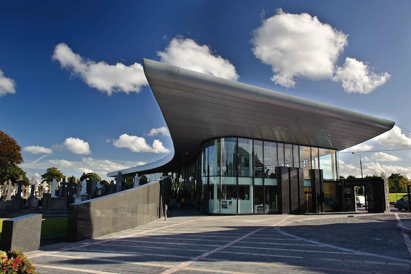 A modern building with a curved roof and glass facade, surrounded by a cemetery. 1
