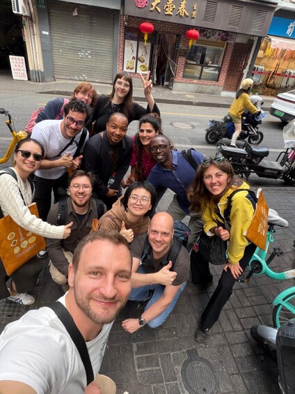 A group of people posing for a photo on a city street with a restaurant and scooters in the background. 2