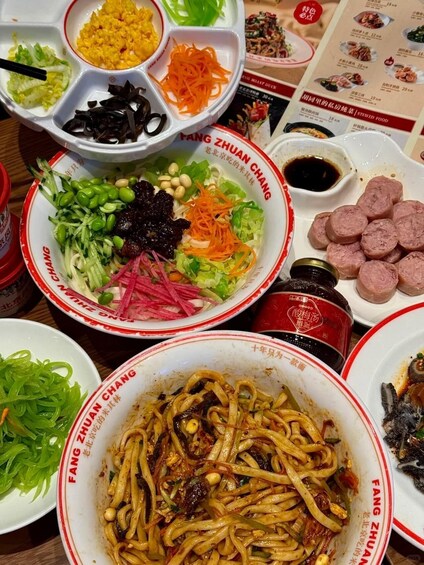 A variety of dishes including noodles, vegetables, and meat, served on a table with a menu in the background. 1