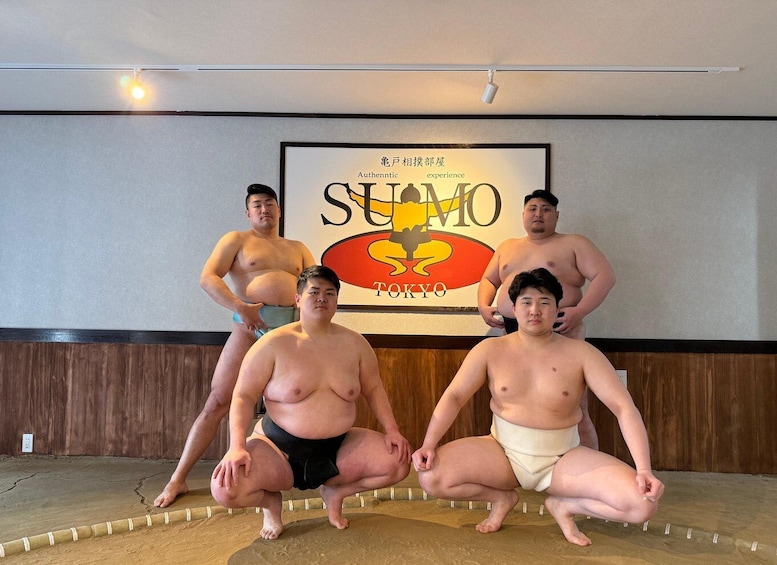 Four sumo wrestlers in a room with a large Sumo sign on the wall. 1