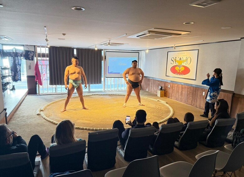 Two sumo wrestlers in a ring with spectators. 5