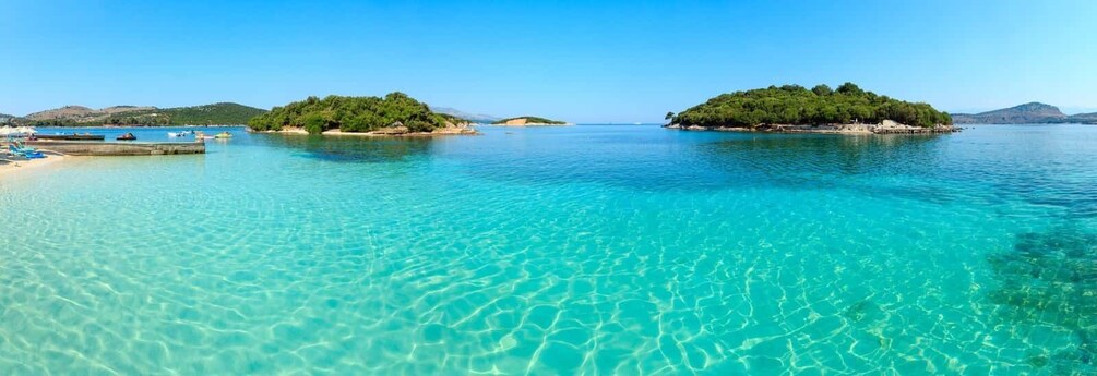 A clear turquoise sea with two small islands, one with a sandy beach and the other with dense greenery. 1